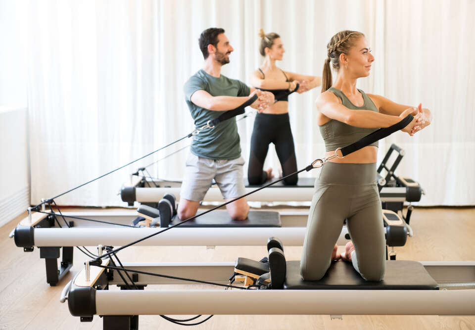 Three people exercising torson rotation at gym using pilates reformer beds
